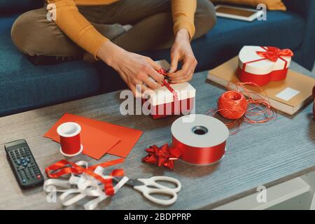 Giovane donna seduta sul divano a casa e la preparazione di bei regali per Natale, vacanze e celebrazione concetto Foto Stock