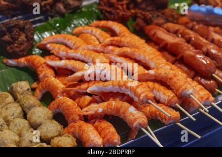 Gamberi, palle di carne e salsicce su bastoni in una teglia sul mercato alimentare di strada a Phuket, Thailandia, primo piano. Foto Stock