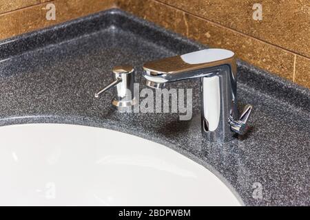 Lavello bianco in marmo marrone con rubinetto cromato lucido e dispenser integrato per sapone liquido Foto Stock