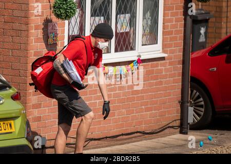 Un postino Royal Mail nei suoi giri durante la chiusura a chiave del coronavirus indossando una maschera facciale, guanti e pantaloncini, aprile 2020. Foto Stock