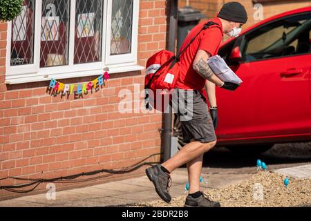 Un postino Royal Mail nei suoi giri durante la chiusura a chiave del coronavirus indossando una maschera facciale, guanti e pantaloncini, aprile 2020. Foto Stock