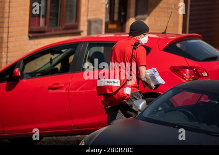 Un postino Royal Mail nei suoi giri durante la chiusura a chiave del coronavirus indossando una maschera facciale, guanti e pantaloncini, aprile 2020. Foto Stock