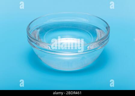 Acqua da bere pura e limpida in una ciotola di vetro o in un piatto su sfondo blu Foto Stock
