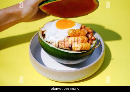 Riso fritto con uova soleggiate e salsiccia in contenitore di anguria con sfondo giallo Foto Stock