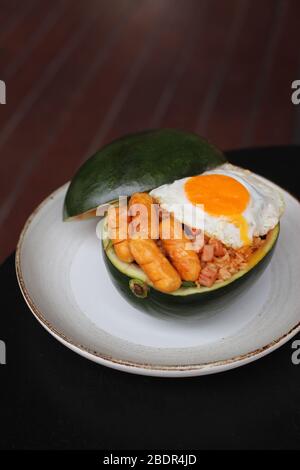 Riso fritto con uovo soleggiato e salsiccia in contenitore di anguria con sfondo giallo Foto Stock