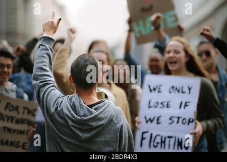 Attivista femminile che gridò su un megaphone in una marcia di protesta. Giovani che protestano con manifesti e megafone. Foto Stock