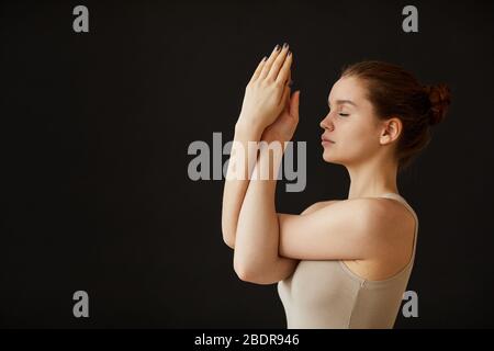 Giovane donna che fa l'esercitazione di rilassamento durante lo yoga su sfondo nero Foto Stock