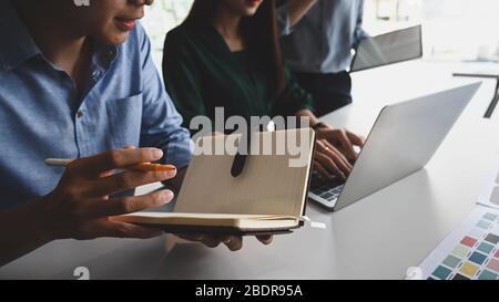 Immagine ritagliata del team di sviluppo aziendale che discute/incontrate/lavora insieme al moderno tavolo da riunione utilizzando un computer portatile e delle note. Colla Foto Stock