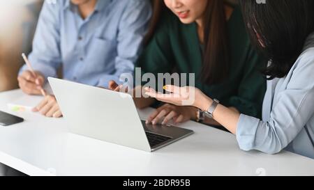 Immagine ritagliata del team di sviluppo aziendale che discute/incontrate/lavora insieme al moderno tavolo da riunione utilizzando un computer portatile e delle note. Colla Foto Stock