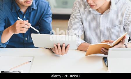 Immagine ritagliata del team di sviluppo aziendale seduto e parlando del loro piano aziendale al moderno tavolo riunioni con comodo ufficio come backgr Foto Stock