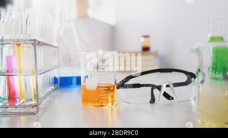 Foto di banco di sperimentazione scientifica con vetreria chimica, pila di libri, liquidi colorati e occhiali di sicurezza che vi mettono sopra. Concetto di wor ordinato Foto Stock