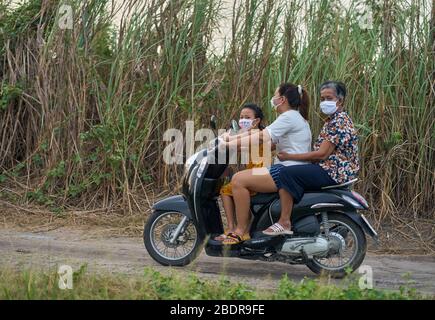 Una famiglia su una moto che indossa maschere facciali a causa del virus Corona, in Thailandia. Foto Stock