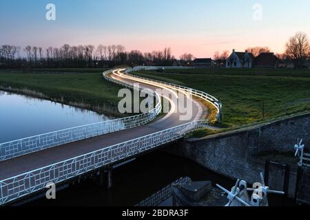 Strada di campagna curva Asphalt nella campagna olandese con recinto bianco che conduce verso un vecchio casale in Olanda. Foto Stock
