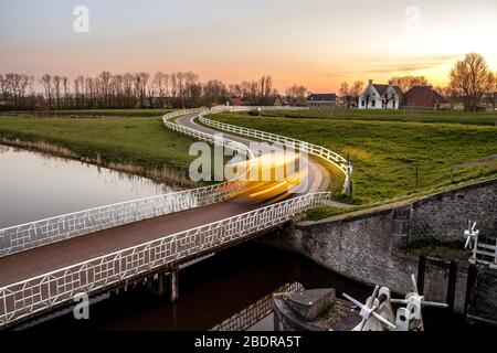 Strada di campagna curva Asphalt nella campagna olandese con recinto bianco che conduce verso un vecchio casale in Olanda. Foto Stock