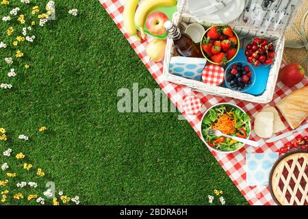 Estate impostazione picnic sul prato con aprire il cestino da picnic, frutta, insalata e torta di ciliegie Foto Stock