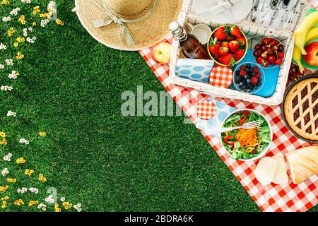 Estate impostazione picnic sul prato con aprire il cestino da picnic, frutta, insalata e torta di ciliegie Foto Stock