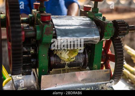 Venditore di strada in India estrazione di succo di canna da zucchero da zucchero utilizzando una macchina spremiagrumi Foto Stock