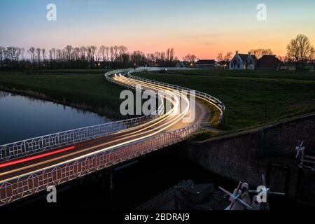 Strada di campagna curva Asphalt nella campagna olandese con recinto bianco che conduce verso un vecchio casale in Olanda. Foto Stock