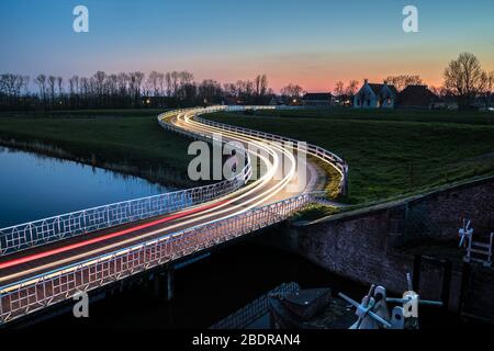 Strada di campagna curva Asphalt nella campagna olandese con recinto bianco che conduce verso un vecchio casale in Olanda. Foto Stock