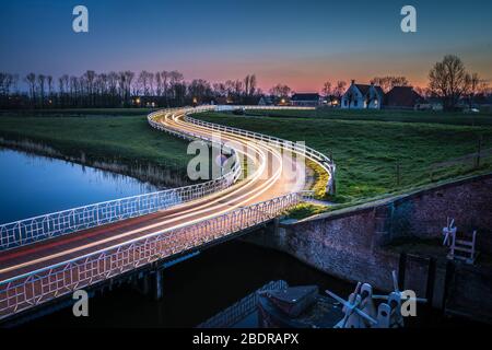 Strada di campagna curva Asphalt nella campagna olandese con recinto bianco che conduce verso un vecchio casale in Olanda. Foto Stock