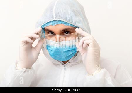 Ritratto di uomo medico indossare googles, glusses protettivo in tuta di protezione, maschera chirurgica viso su sfondo bianco. Concetto di assistenza sanitaria medica Foto Stock