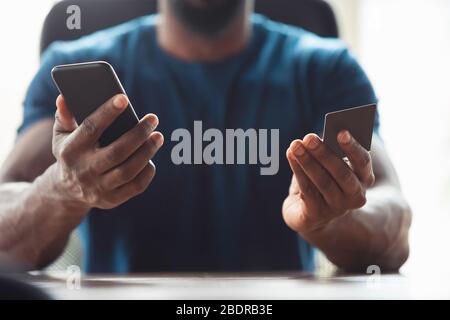 Primo piano di mani maschili afro-americane, in carica. Concetto di business, finanza, lavoro, shopping online o vendite. CopySpace per la pubblicità. Istruzione e freelance. Telefono e carta di credito. Foto Stock