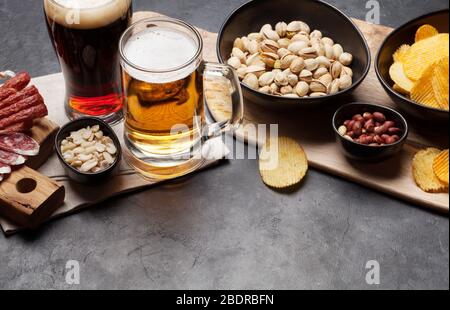 Birra alla spina e spuntini su sfondo di pietra. Noci, patatine, salsicce Foto Stock