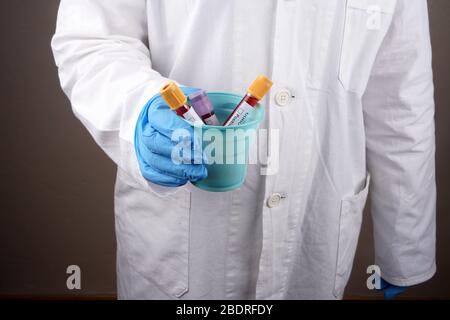 Il medico tiene le provette di sangue in una tazza di plastica Foto Stock