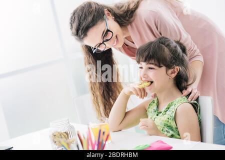 Carina ragazza in età prescolare avente uno snack con la madre, si è mangiare alcuni deliziosi biscotti, nutrizione e concetto di stile di vita Foto Stock