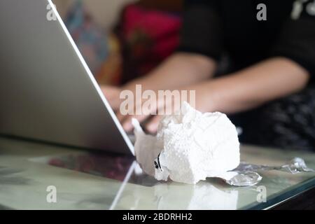 Giovane donna indiana che lavora su un computer portatile mentre ammalato con tessuti bianchi e medicina in lamina d'argento nelle vicinanze Foto Stock