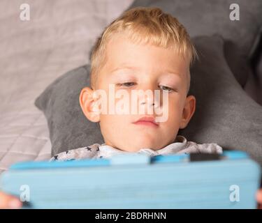 Bambino caucasico che usa un tablet digitale mentre si stese a letto a casa Foto Stock