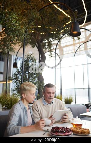 Coppia matura seduta al tavolo e utilizzando il tablet digitale insieme mentre si gustano la colazione in un bar Foto Stock