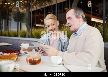 Sorridente coppia matura guardando qualcosa su tablet digitale mentre beve il tè al ristorante Foto Stock
