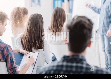 Seminario di affari e presentazione, un uomo sta dando un colloquio e il pubblico sta ascoltando e scrivendo le note Foto Stock