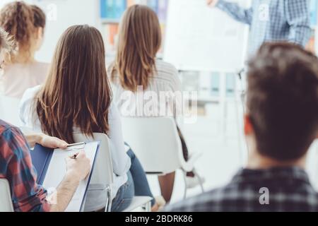 Seminario di affari e presentazione, un uomo sta dando un colloquio e il pubblico sta ascoltando e scrivendo le note Foto Stock