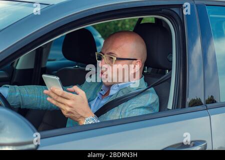 Incidente di uomo che usa il telefono durante la guida. Closeup ritratto ritagliato immagine orizzontale di scioccato uomo d'affari, conducente che tiene utilizzando il telefono di SMS Foto Stock