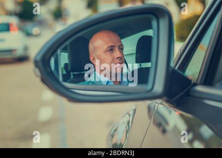 Un giovane uomo d'affari, un bel pilota sicuro nella sua auto che guarda al riflesso dello specchietto retrovisore esterno. Emozioni positive di espressione del volto umano. Sicuro Foto Stock