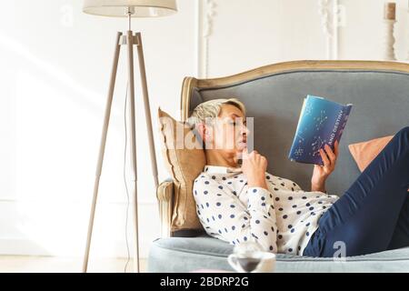 Donna bionda focalizzata che legge un libro di astrologia Foto Stock