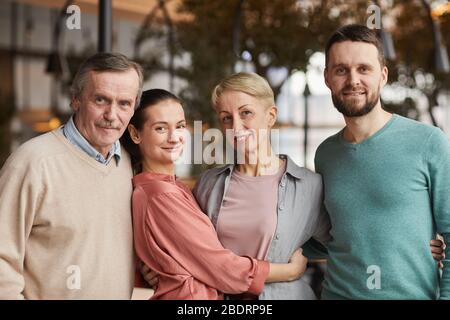 Ritratto di famiglia di quattro persone che si abbracciano e sorridono a macchina fotografica mentre si trova al ristorante Foto Stock
