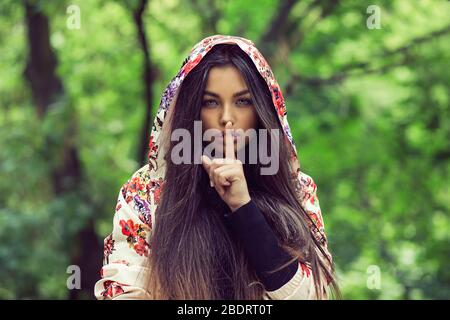 Donna con occhi spalancati che chiede silenzio o segretezza con il dito sulle labbra hush mano gesto verde fondo muro. Bella ragazza carina che mette le dita sulle labbra, s Foto Stock