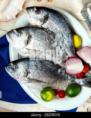 tre pesce crudo messo su piatto con pomodoro di ciliegia di cipolla e ghiaccio Foto Stock
