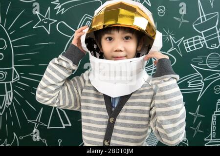 Indossando un casco di astronauti, il ragazzino si trova davanti alla lavagna Foto Stock