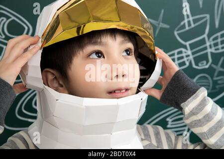 Indossando un casco di astronauti, il ragazzino si trova davanti alla lavagna Foto Stock