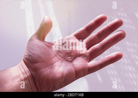 Un uomo che usa gel disinfettante idroalcolico, cadendo da una bottiglia sulla sua mano. Retroilluminazione dal sole Foto Stock