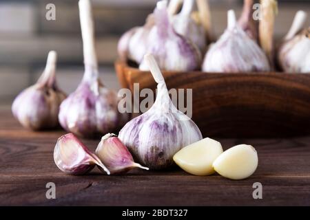 Bulbi e spicchi d'aglio in una ciotola di legno vintage su sfondo scuro Foto Stock