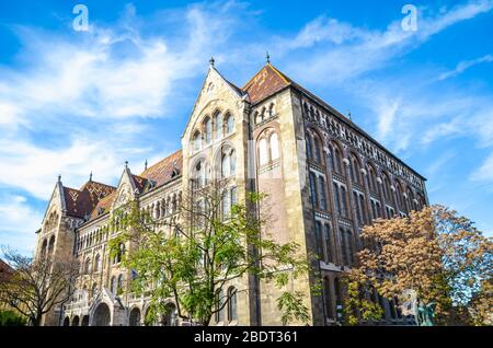 Il bellissimo edificio storico dell'Archivio Nazionale Ungherese nella capitale ungherese Budapest. L'esterno della casa circondata da alberi su una foto orizzontale con cielo blu sopra. Foto Stock