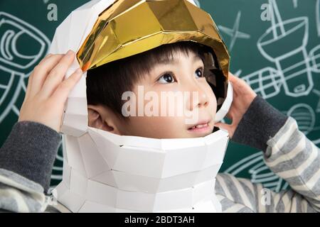 Indossando un casco di astronauti, il ragazzino si trova davanti alla lavagna Foto Stock