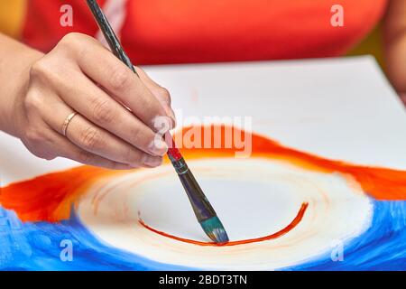 Artista dipinge paesaggio in gouache utilizzando un pennello. La mano della donna tiene il pennello. Primo piano, messa a fuoco selettiva Foto Stock