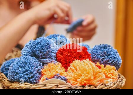 Un cesto con pompons fatti a mano. Il processo di fare i pompons dai fili dalla donna sullo sfondo. Foto Stock