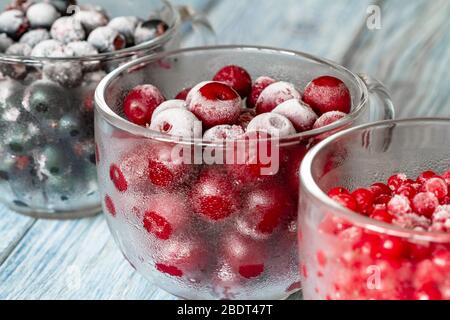 Ciliegie dolci congelate mature, ribes rosso e ribes nero con brina nelle tazze di vetro trasparente su sfondo di legno blu. Naturale guarigione organica Foto Stock